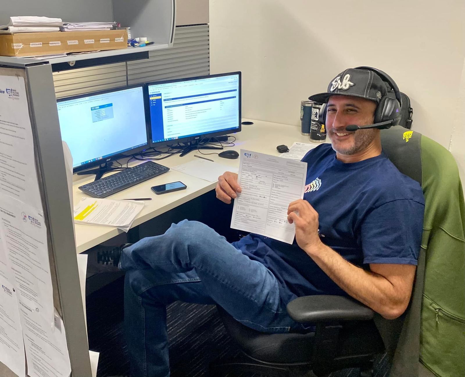 A Senior Solutions agent on a headset at his desk, holding up a completed application