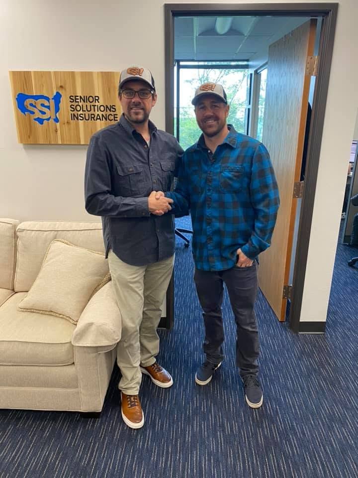 A handshake under the Senior Solutions Insurance sign